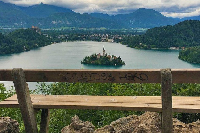 Un banco de madera con vista a un lago, una pequeña isla y montañas al fondo. 2