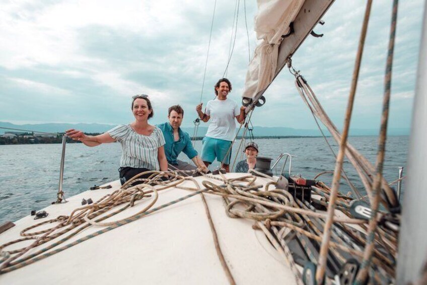 A sailboat with people on deck, ropes, and a body of water in the background. 1