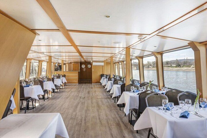 A dining area on a boat with tables set for a meal, wooden walls, and a view of the water. 3