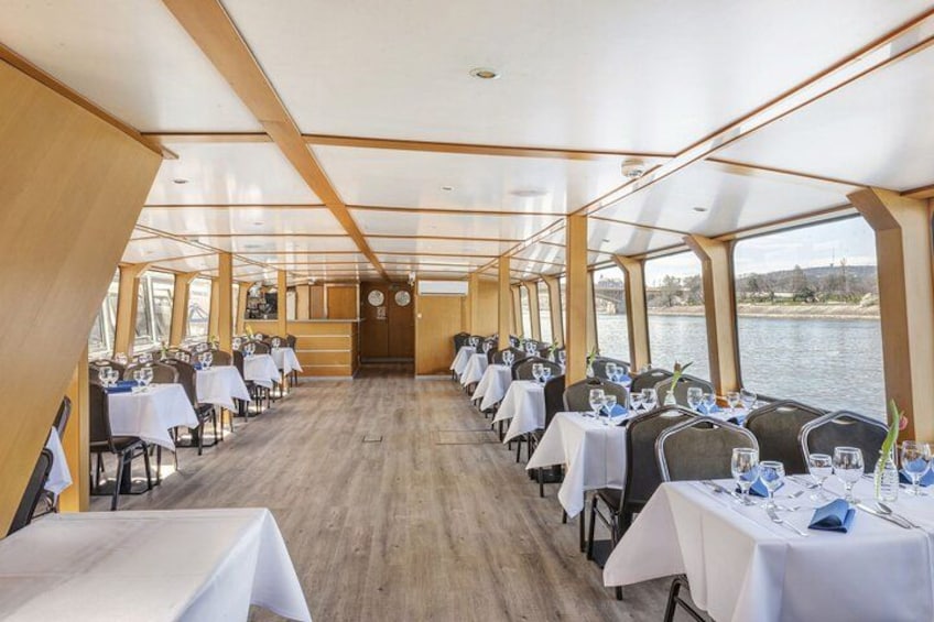 Comedor en un barco con mesas dispuestas para una comida, ventanas amplias y vista al agua. 3