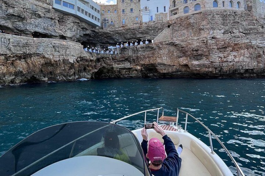 A boat with a person wearing a pink cap, a rocky coastline, and a building with multiple windows. 3