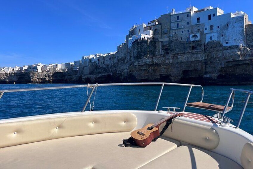 A boat with a guitar on the bow, water, and a coastal town with white buildings. 5