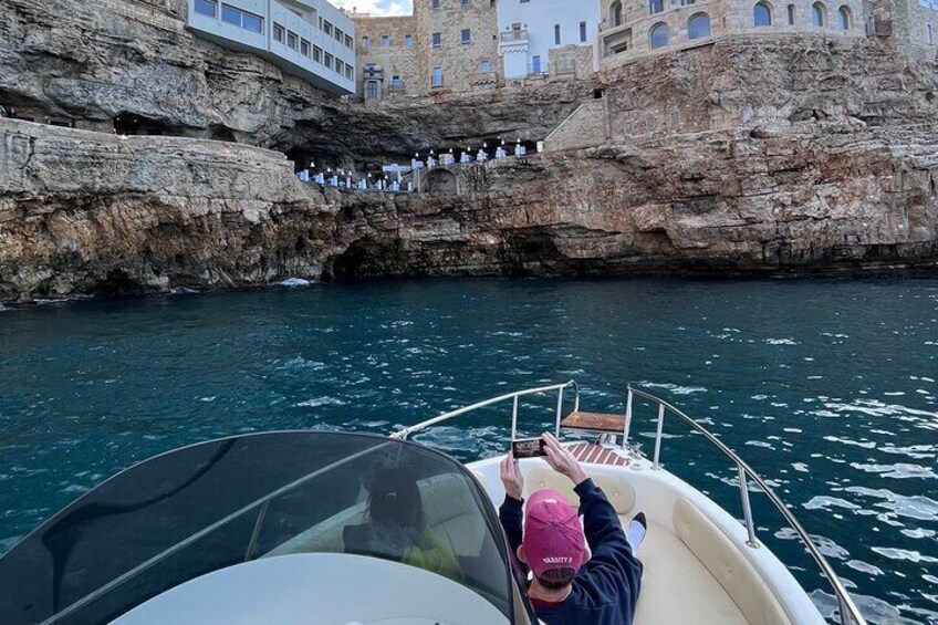 A boat with a person wearing a pink cap, a rocky coastline, and a building with steps leading up to it. 3