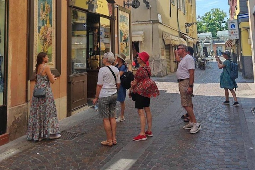 Des personnes se tiennent debout sur une rue pavée, devant une boutique dont la vitrine est en verre, et on aperçoit un panneau de signalisation. 4