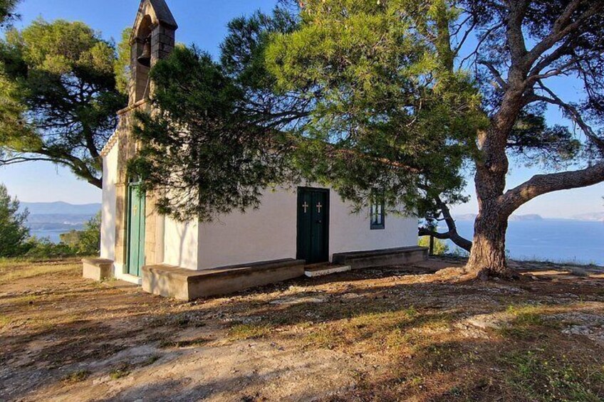 A small white church with a green door and a bell tower, surrounded by trees and a clear sky. 3