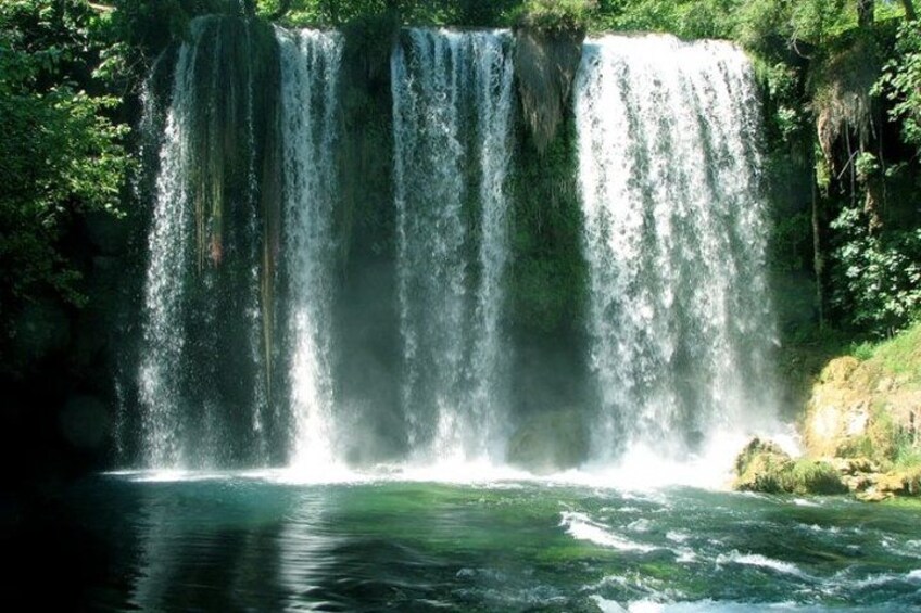 Ein Wasserfall stürzt in einen Fluss, umgeben von dichtem Grün. 3