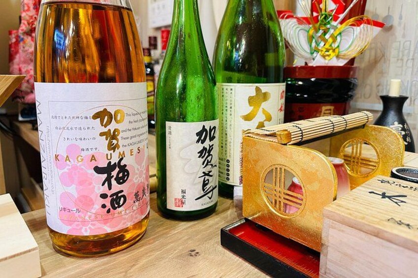 Botellas de sake con etiquetas japonesas, un pincel de bambú y un bloque de madera con caligrafía. 2