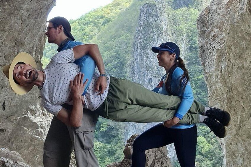 A person being carried by another on a rocky cliff with a forested valley in the background. 2