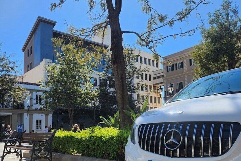 A white car parked in front of a building with a blue facade, a tree, and a bench. 4