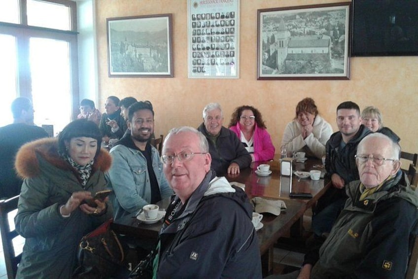 En grupp människor sitter vid ett bord på ett kafé. Det finns en menytavla och inramade bilder på väggen. 3