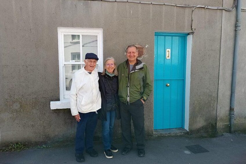 Tres personas de pie frente a un edificio con una puerta azul y una ventana. 2