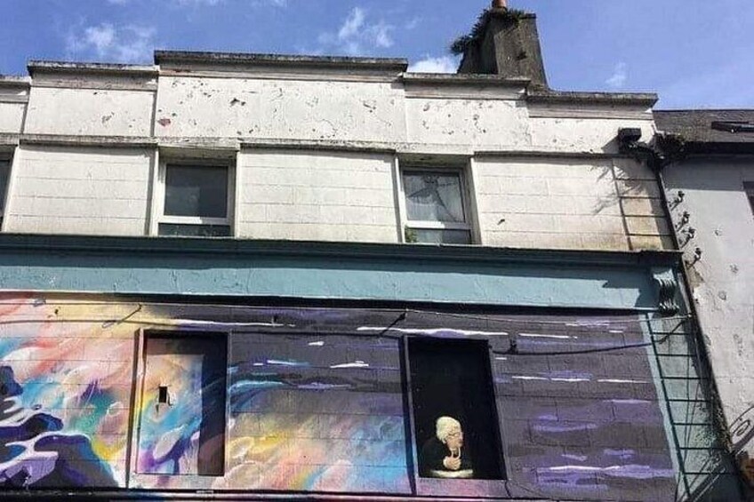 Un bâtiment dont la partie inférieure de la façade est ornée de graffitis et dans lequel on peut apercevoir une sculpture en buste à travers une fenêtre. 1