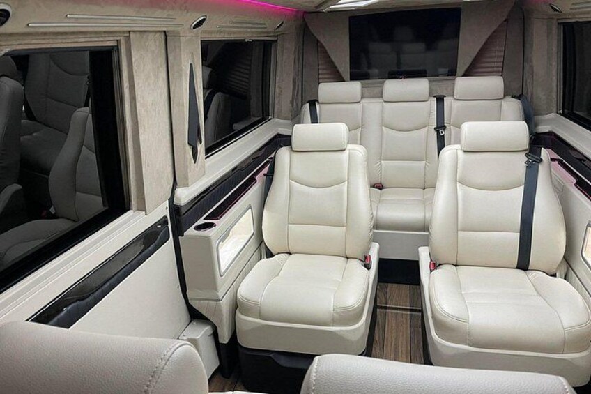 A luxury RV interior with beige leather seats and a central aisle. 2