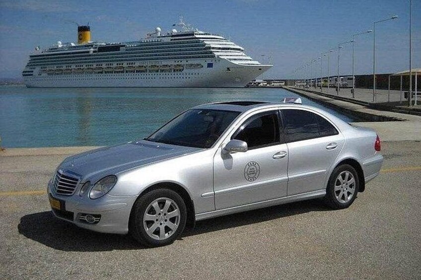 A silver sedan parked near a waterfront with a cruise ship in the background. 3