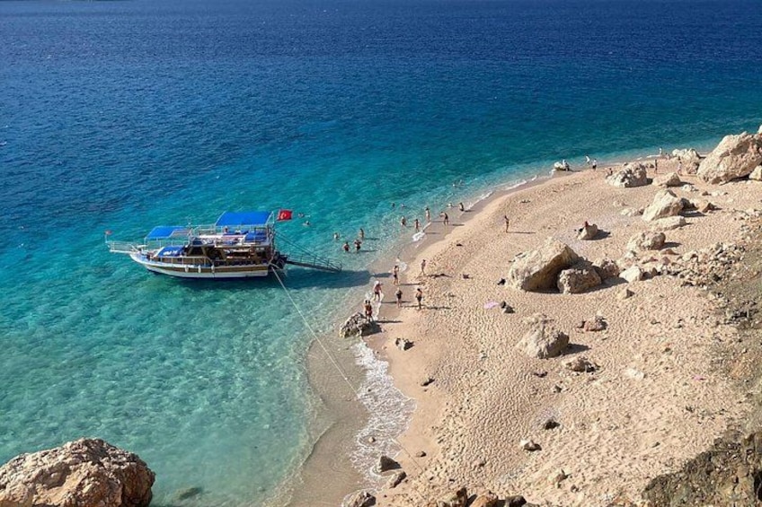 A beach with clear turquoise water, a boat anchored near the shore, and rocky terrain. 2