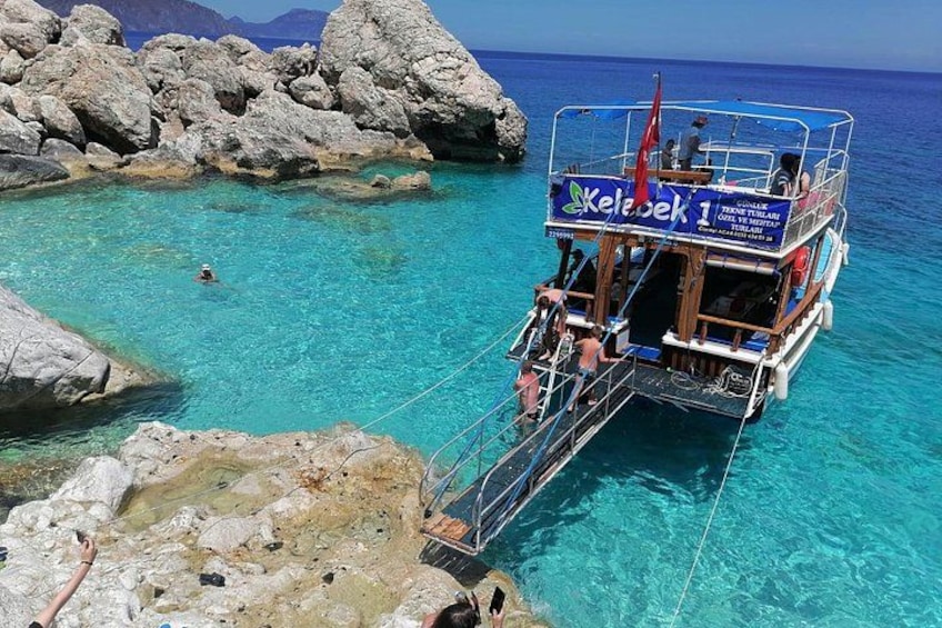 A boat named 'Kelebek 1' docked at a rocky shore with clear turquoise water. 5