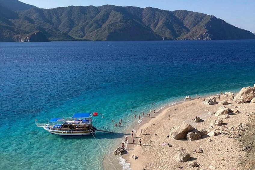 A boat on a clear blue sea, a rocky beach, and mountains in the background. 4