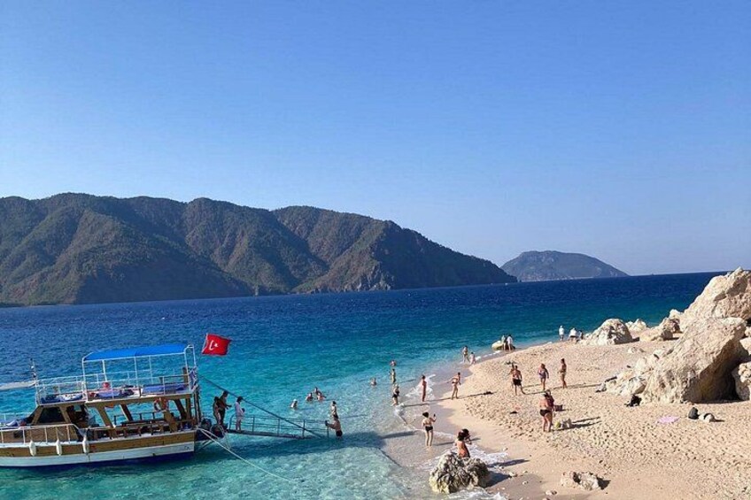 A beach with clear turquoise water, people sunbathing, and a boat with a flag. 3