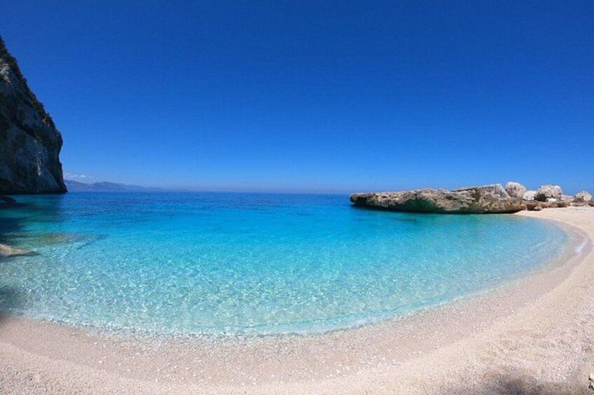 A clear blue sea, sandy beach, and rocky outcrops. 3
