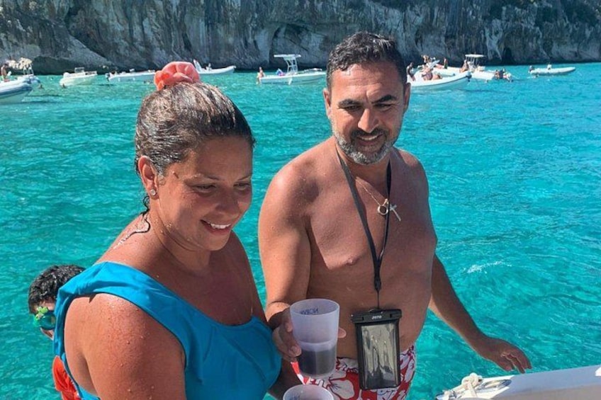 Dos personas en un bote, con agua turquesa cristalina y acantilados rocosos al fondo. 2