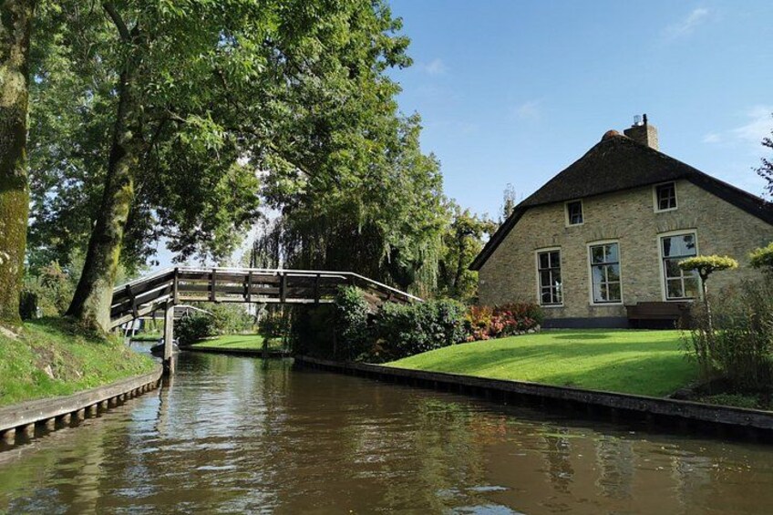 Une maison en pierre avec un pont en bois enjambant un canal, le tout entouré d’une végétation luxuriante. 3