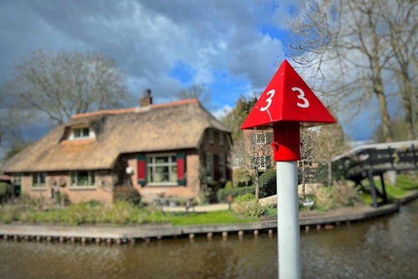 Une maison à toit de chaume, un canal et un panneau triangulaire rouge portant le chiffre 3. 2