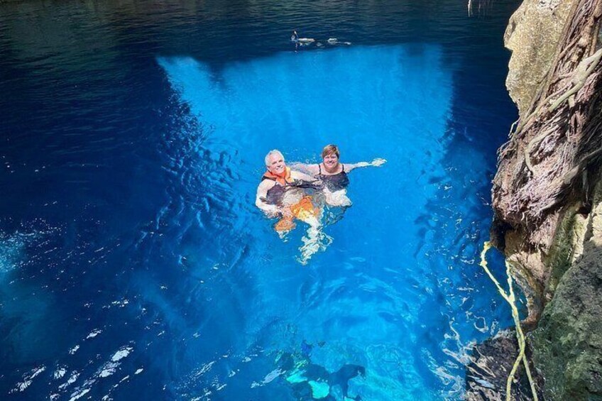 Two people swimming in a clear blue pool surrounded by rocky cliffs. 3