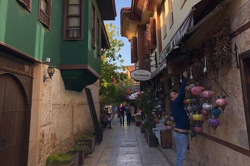 A narrow street with buildings on either side, a shop with a sign reading 'Hadrian,' and hanging decorative lanterns. 3