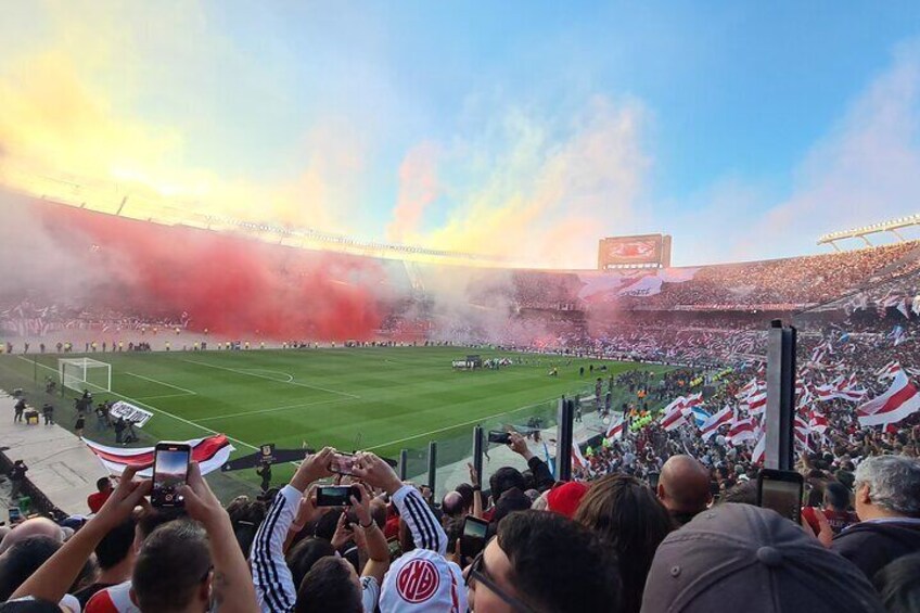 A stadium filled with spectators, some holding flags, and smoke in the air. 4