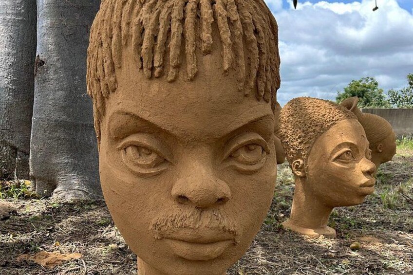 Escultura de una persona con cabello trenzado, ubicada al aire libre con árboles y un cielo nublado de fondo. 4