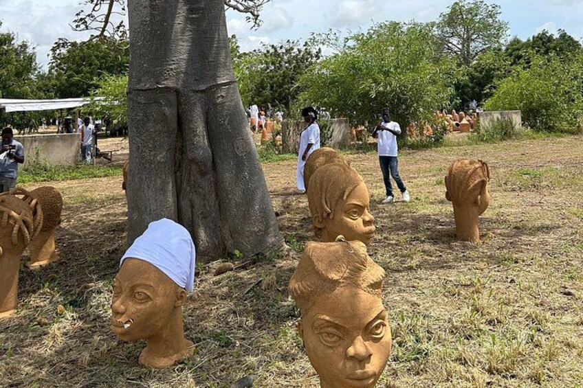 Esculturas de terracota con forma de cabeza humana en un entorno al aire libre, con árboles y gente de fondo. 5
