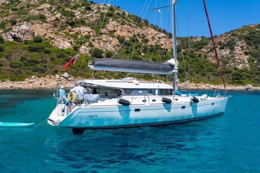 Una barca a vela con lo scafo bianco e una bandiera rossa, ancorata vicino a colline rocciose e acque cristalline. 1