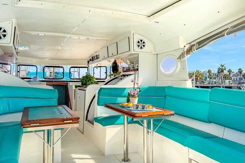 A boat interior with teal seating, a table, and a potted plant. 5