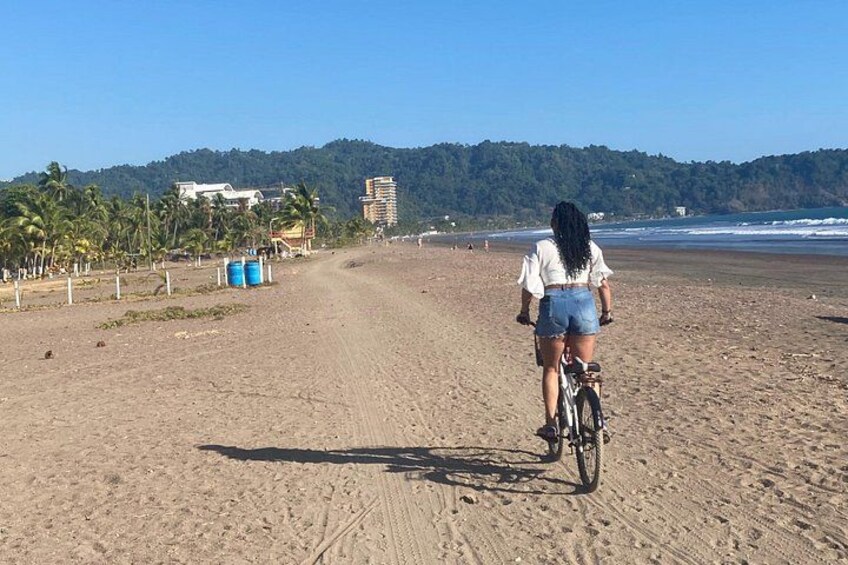 A sandy beach with a person riding a bicycle, palm trees, and buildings in the background. 5