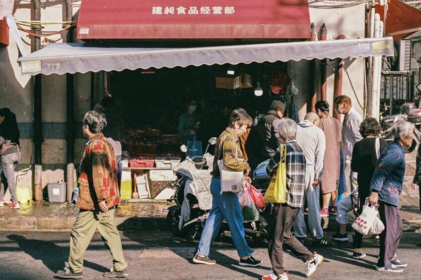 A street scene with people walking past a shop with a red awning. 2