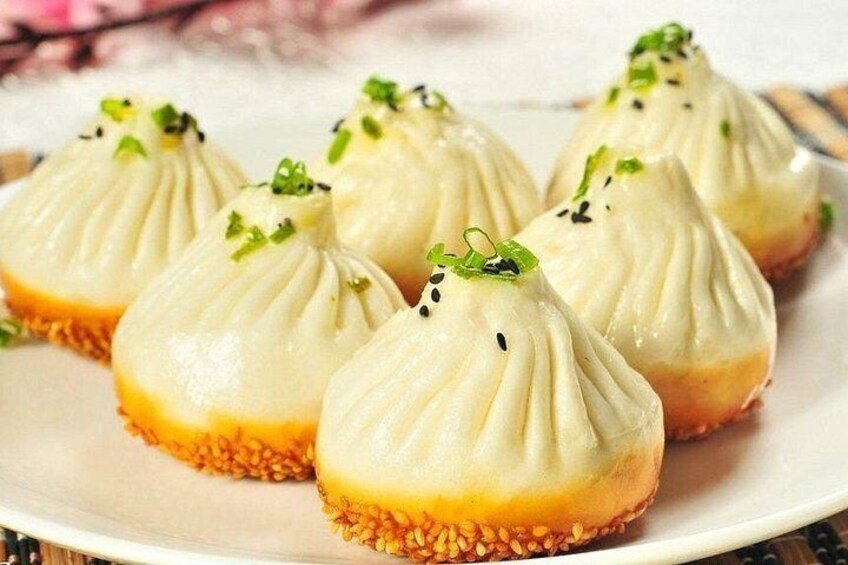 A plate of steamed buns with sesame seeds and green garnish. 4