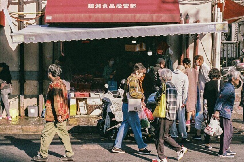 A street scene with people walking and standing in front of a shop with a red awning. 5