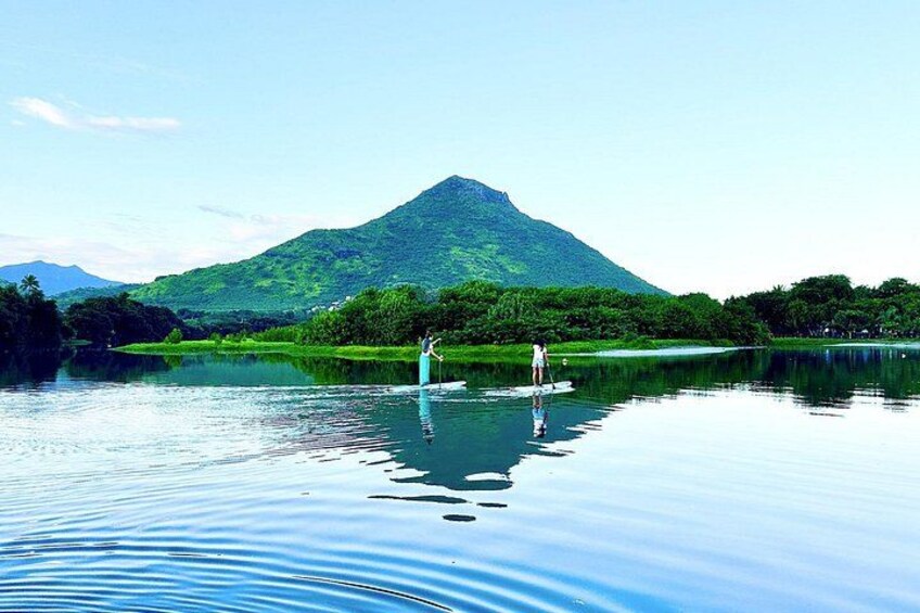 Un lac paisible où deux personnes pratiquent le paddle, entouré d’une végétation luxuriante et avec une montagne en arrière-plan. 5