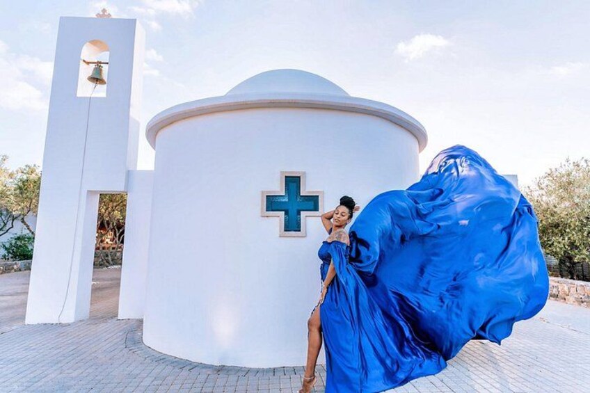 A white building with a cross symbol, a bell tower, and a person in a blue dress. 1