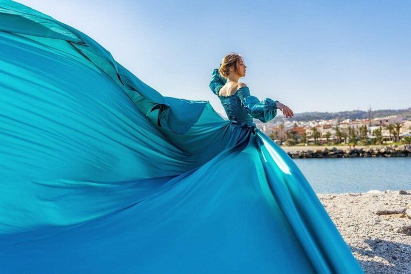A person in a flowing blue dress by a waterfront with buildings in the background. 4