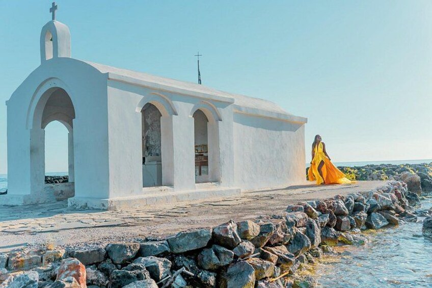 A white church with a cross on top, a rocky shoreline, and a person in a yellow dress. 5