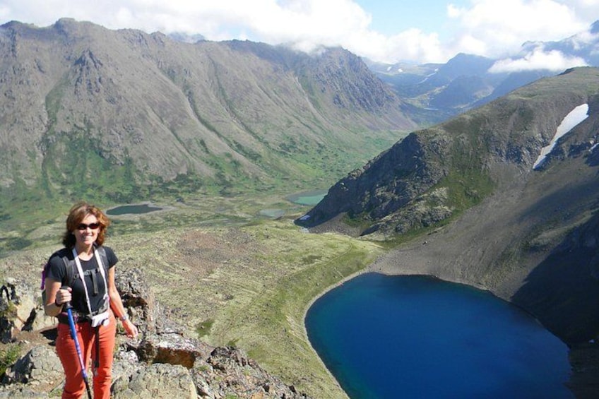 A hiker on a mountain trail overlooking a lake and mountains. 1