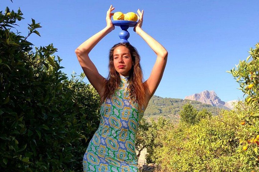 Una persona equilibra frutas en la cabeza en un jardín con árboles y una montaña al fondo. 2