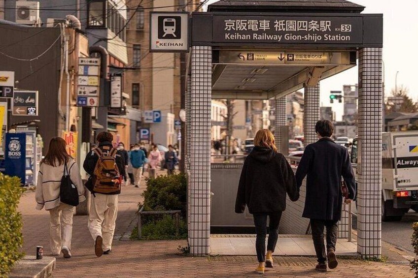 Ein Fußweg mit einer gefliesten Konstruktion, Hinweisschildern für die Keihan Railway Gion-shijo Station und Fußgängern. 2