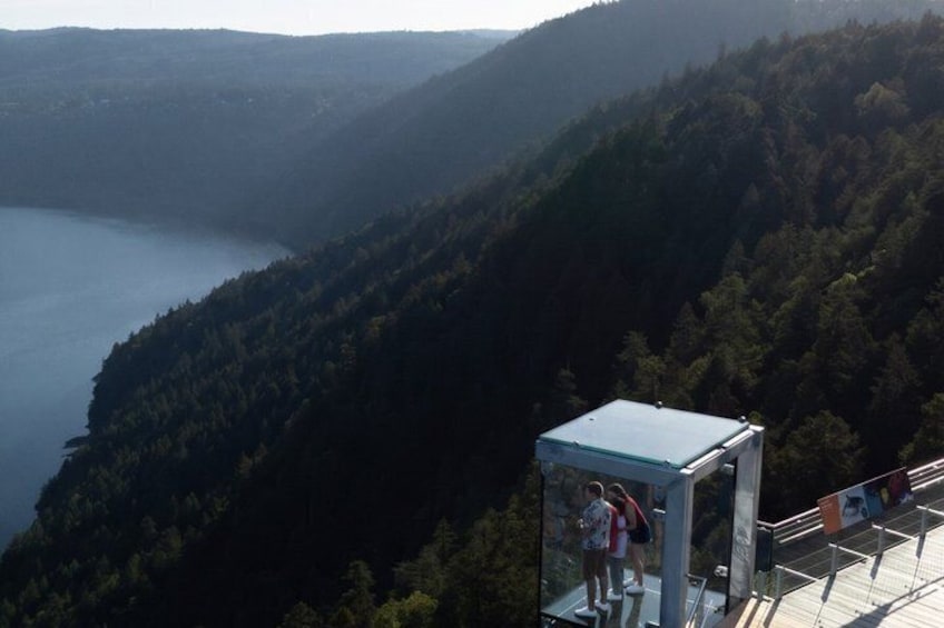 A glass observation tower overlooking a lake and forested mountains. 4