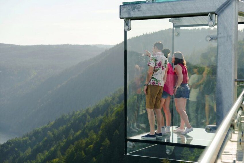 A glass observation platform with people looking at a mountainous landscape. 5
