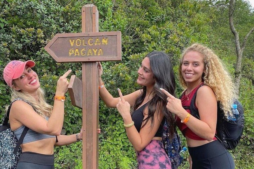 Drie personen wijzen naar een houten bord met de tekst 'VOLCANO PACAYA'. 4