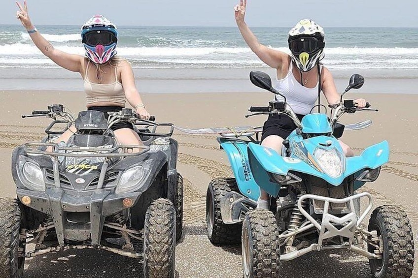 Two people on ATVs on a beach with ocean in the background. 2