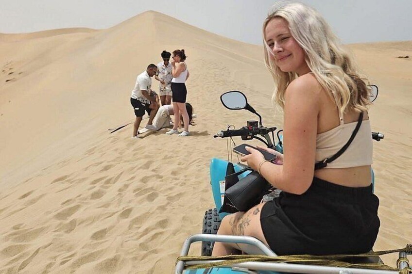 A person on a dune buggy, a group of people on the sand, and sand dunes in the background. 3