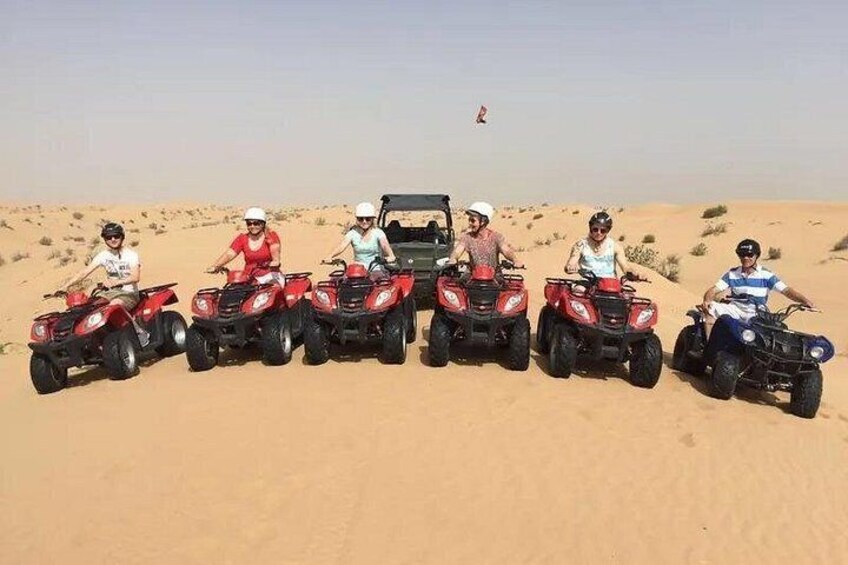 Five people on red ATVs in a desert with sand dunes. 1